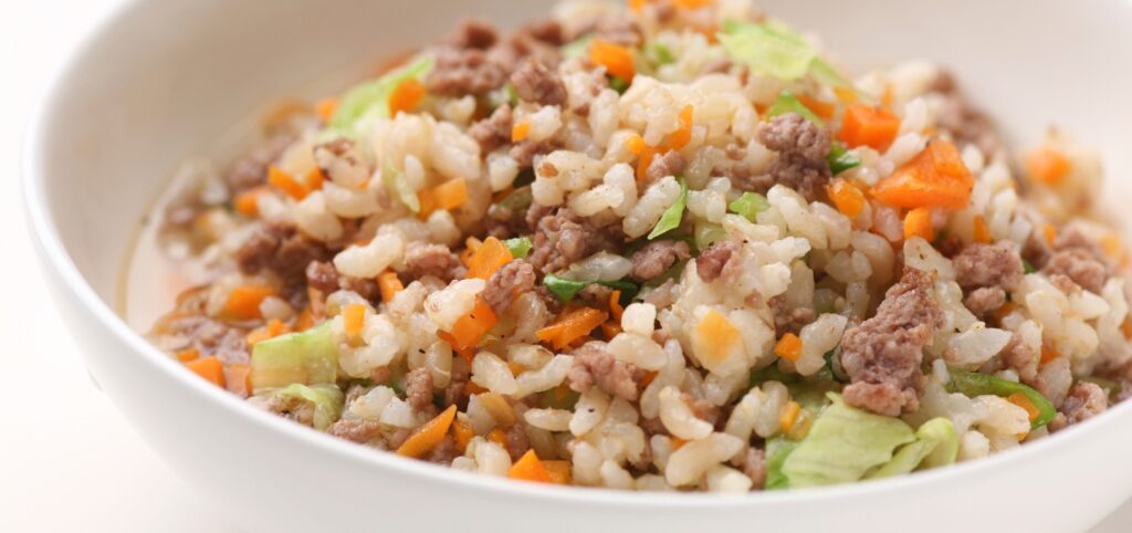 Eine Schüssel gefüllt mit gekochtem Reis, Karotten und Fleisch.